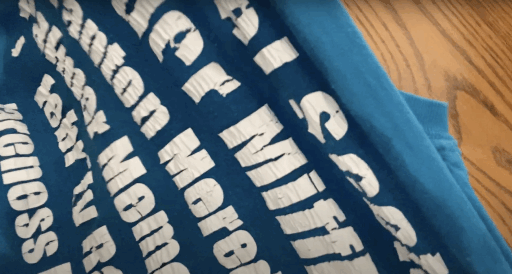 Close-up of cracked white iron on vinyl letters on a blue shirt before removal