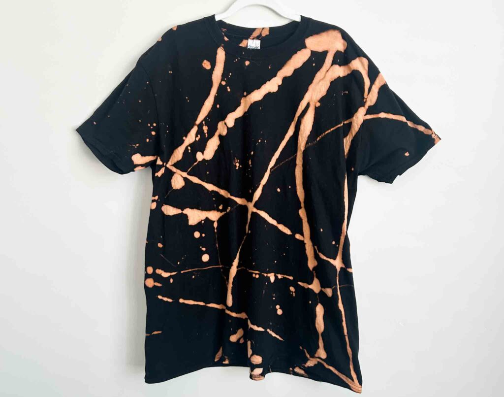 Front view of a black cotton t-shirt reverse tie dyed with toilet bowl cleaner, featuring bold coppery orange splatter and line designs