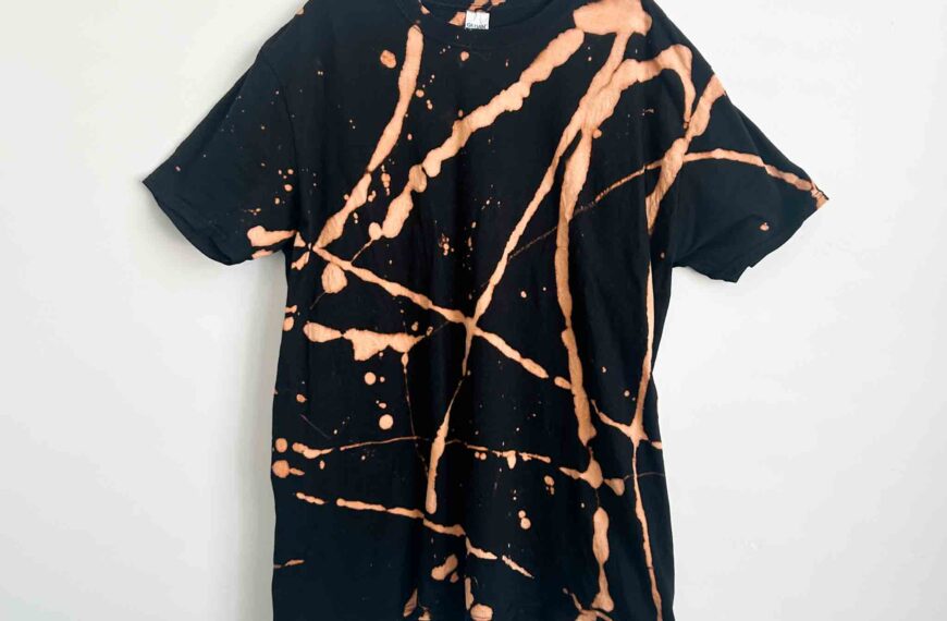 Front view of a black cotton t-shirt reverse tie dyed with toilet bowl cleaner, featuring bold coppery orange splatter and line designs