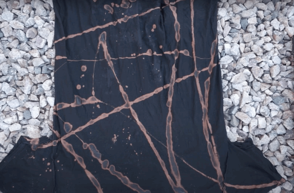 Black shirt after reverse dyeing with toilet bowl cleaner showing orange bleach patterns