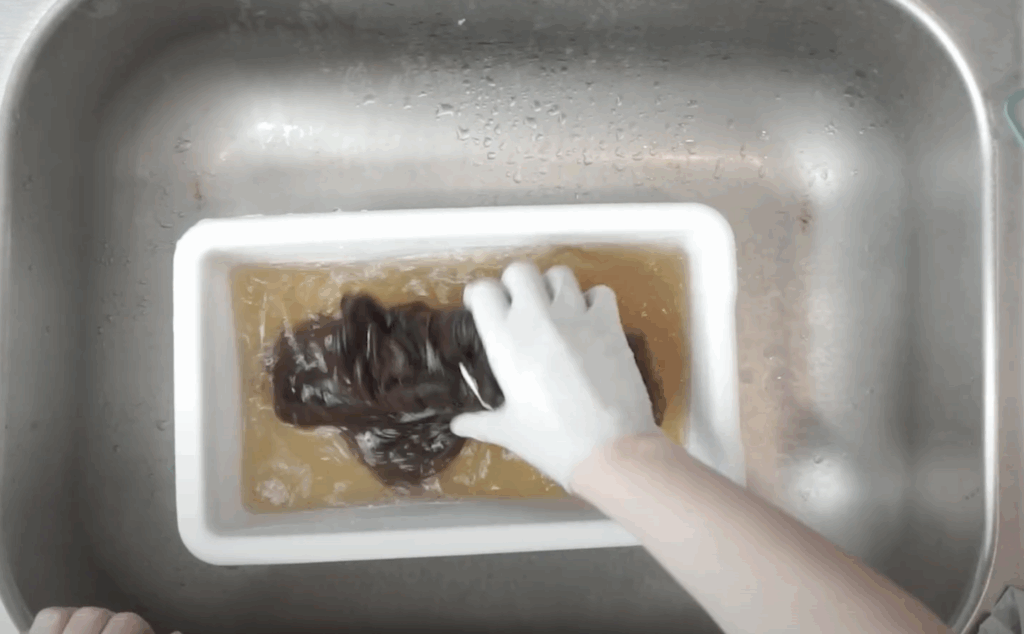 "Gloved hand soaking black shirt in bleach neutralizer bath after reverse dyeing