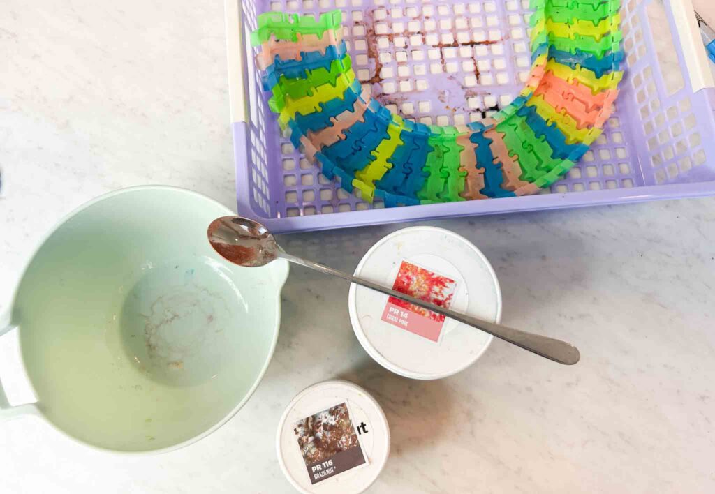 Tie dye setup with Dharma dyes, mixing bowl, spoon, and plastic basket with colorful clips