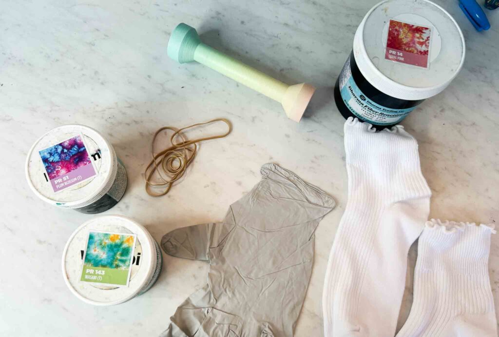 Tie dye supplies on table: gloves, rubber bands, white socks, and Dharma powder dyes