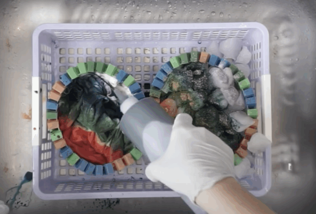 Hand applying liquid dye onto folded fabric in basket while ice melts with dye on the other side, showing side-by-side liquid vs ice tie-dye techniques.