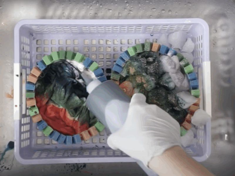 Hand applying liquid dye onto folded fabric in basket while ice melts with dye on the other side, showing side-by-side liquid vs ice tie-dye techniques.