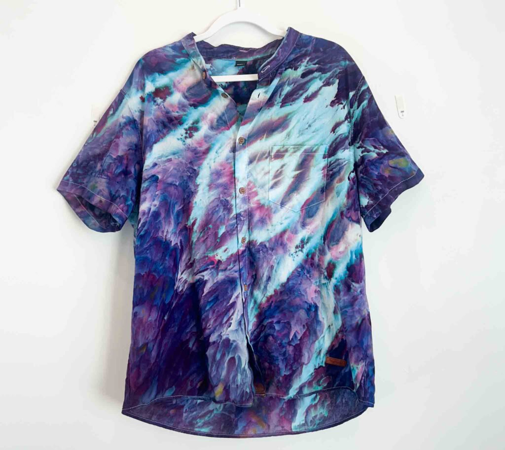 Short sleeve button-up shirt with gravity tie dye design in purple, teal, and white.