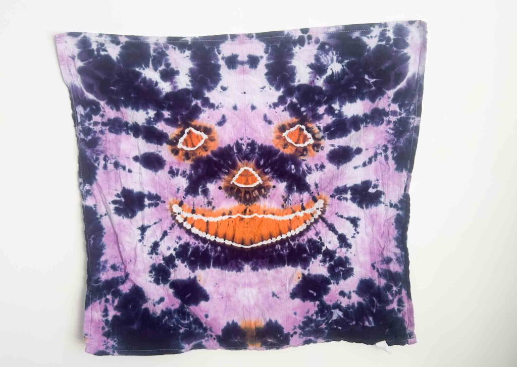 Finished jack-o’-lantern tie dye towel with orange pumpkin face and purple background created using hot water method