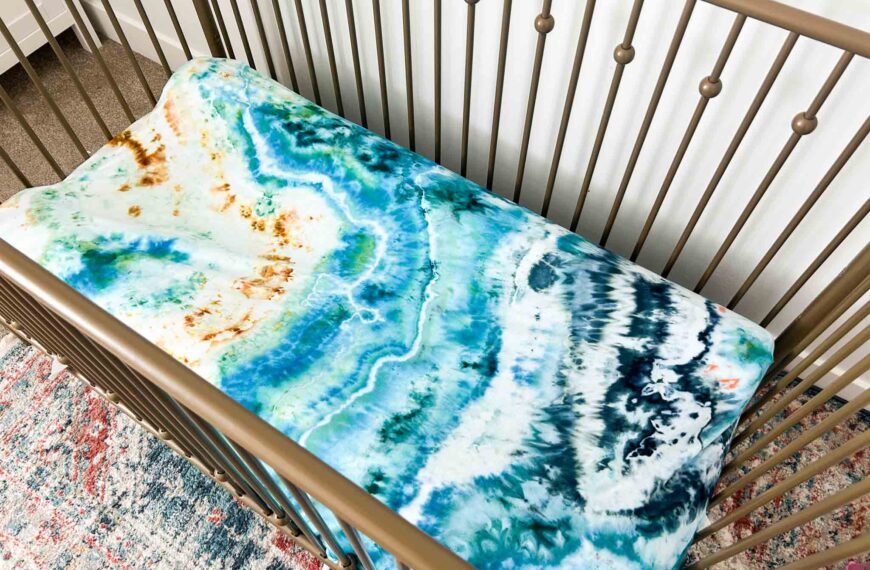 Ocean-inspired geode tie dye crib sheet with shades of teal, blue, and sand inside a modern baby crib.