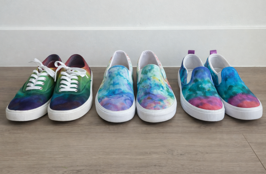 Tie dye shoes comparison showing three pairs of canvas shoes dyed using Sharpie, ice dye, and shaving cream techniques arranged side by side on a wooden floor.