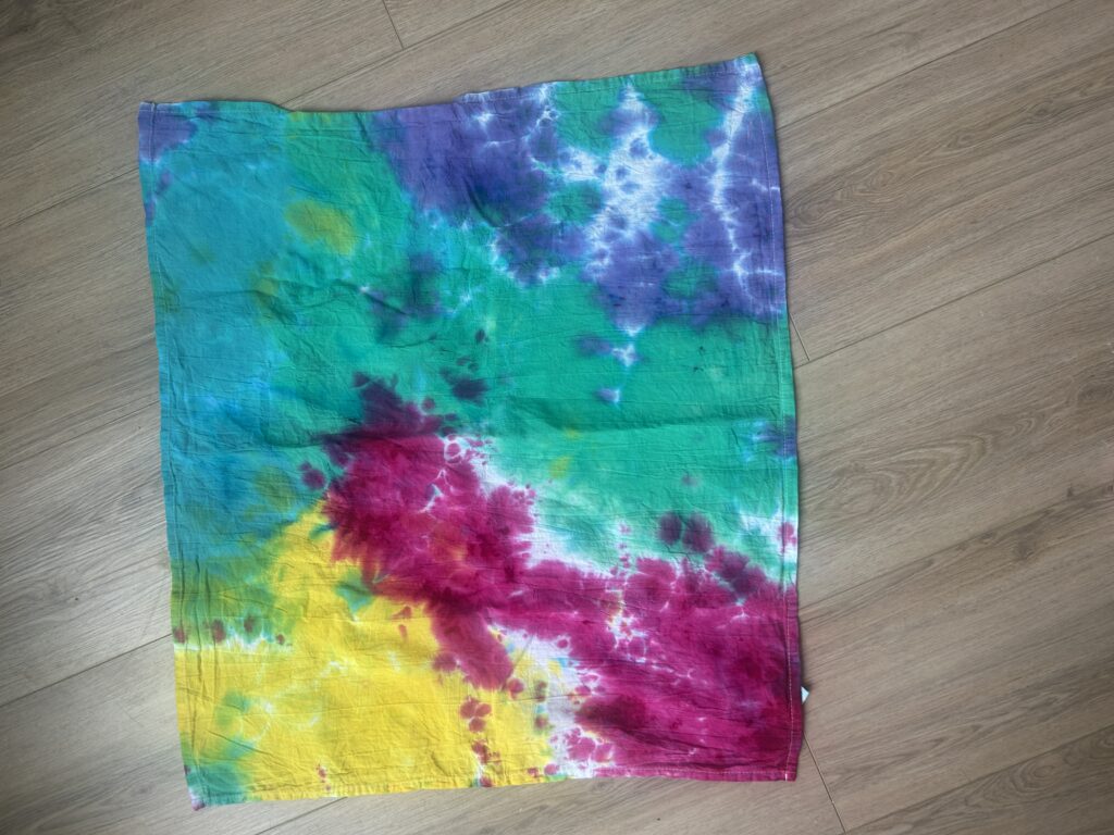 Tie dye tea towel rinsed after 12 hours of liquid dye batching showing moderate color blending and balanced saturation between magenta, yellow, teal, and purple