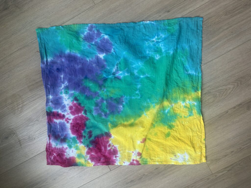 Tie dye tea towel rinsed after 24 hours of liquid dye batching showing fully saturated soft watercolor blending with minimal white space between purple, magenta, yellow, and teal