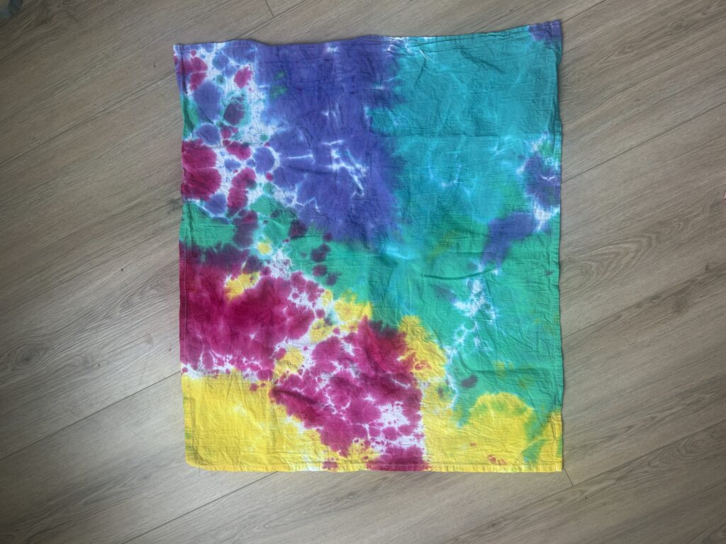 Tie dye tea towel rinsed after 6 hours of liquid dye batching showing crisp white space and bold contrast between magenta, yellow, teal green, and purple