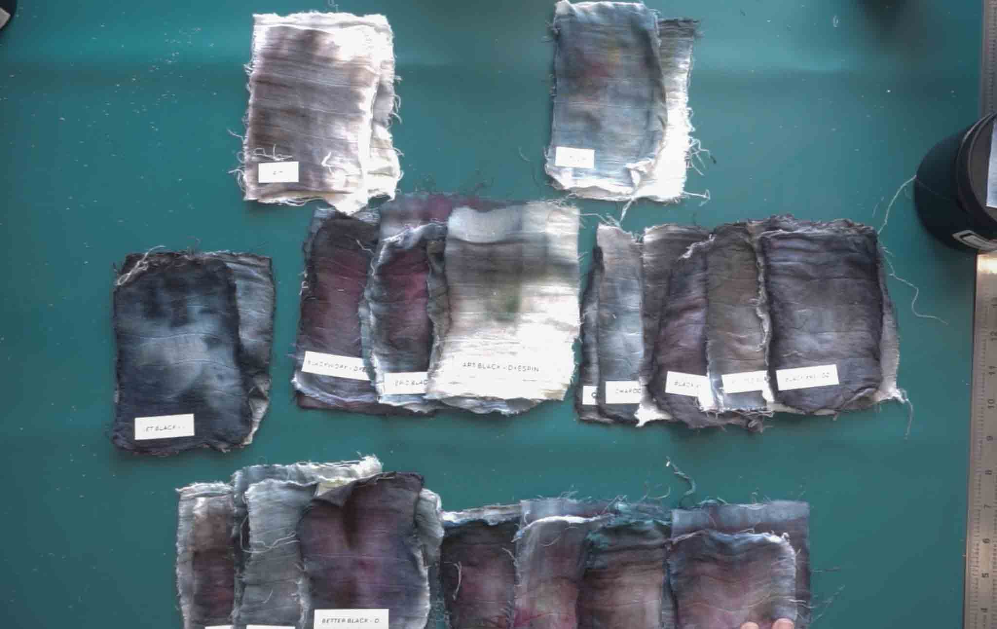 Multiple labeled black ice dye swatches spread across a teal surface showing the full range of results from all brands tested including Jacquard, DyeSpin, Dharma, and Grateful Dyes