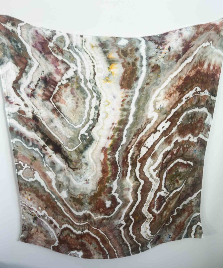 Large piece of geode ice dyed fabric in muted brown, gray, olive, and white tones hung against a white wall