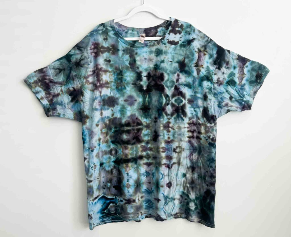 Ice dye glitch fold t-shirt with repeating geometric pattern in teal, navy, and black