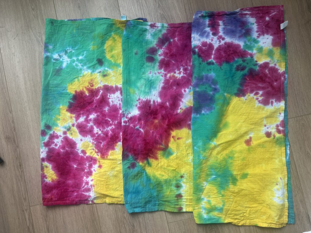 Side by side comparison of three tie dye tea towels labeled 6, 12, and 24 hours showing how liquid dye batching time affects color saturation and white space