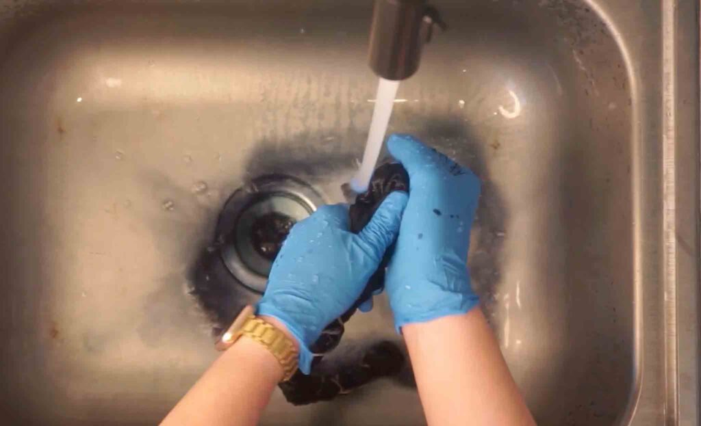 Rinsing excess black dye out of tied mickey tie dye shirt under running water in sink
