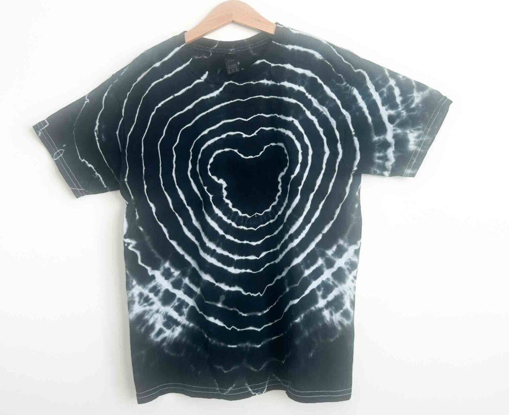 Finished black Mickey Mouse tie dye shirt with white bullseye rings on wooden hanger