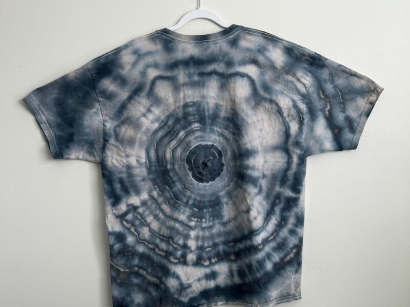 Back of a blue-grey ice dye bullseye t-shirt with soft, watercolor-style concentric rings around a center point.