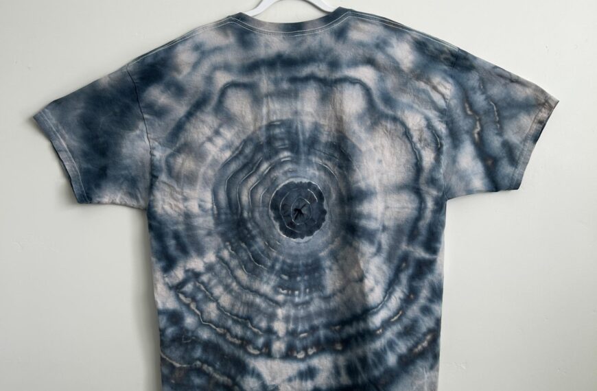 Back of a blue-grey ice dye bullseye t-shirt with soft, watercolor-style concentric rings around a center point.