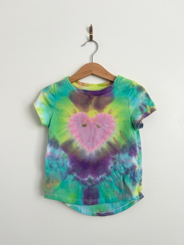 Pink heart tie dye t-shirt with green, purple, and yellow background made with the Create Basics tie dye party tub