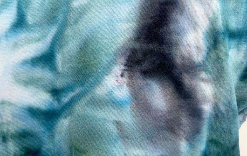 Close-up of soda ash burn on a Tultex white t-shirt after tie dyeing, showing white speckled fiber damage on blue and teal dye