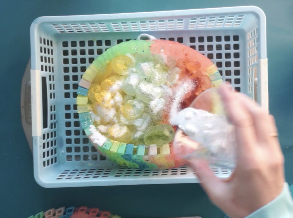Adding dye powder over a hat covered in ice in a basket for ice dyeing