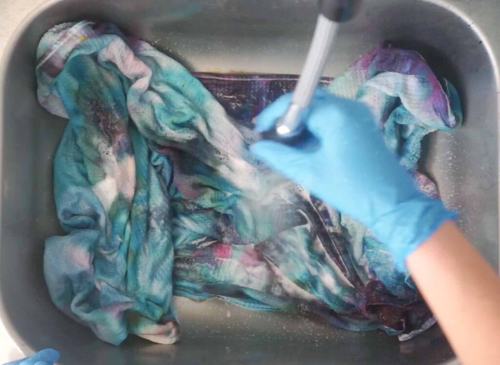 Rinsing a finished teal and purple tie dye beach towel in the sink