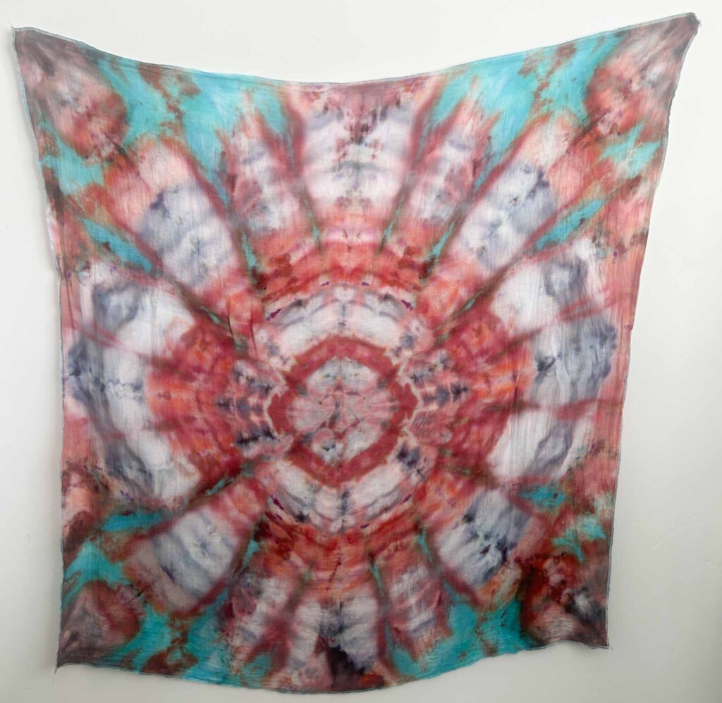 Kaleidoscope tie dye pattern in teal, coral, and white radiating from the center of the fabric