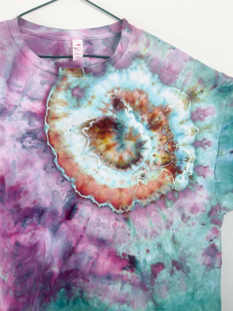 Close-up of a nautilus tie dye spiral pattern in teal, orange, and purple on a t-shirt