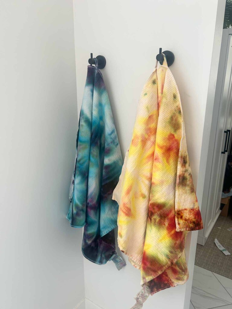 Cool toned and warm toned tie dye beach towels hanging side by side on wall hooks