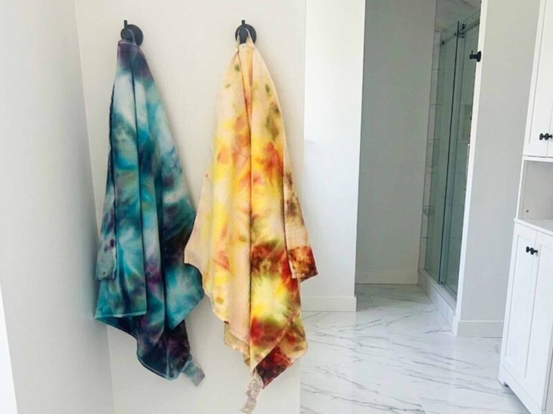 Cool toned and warm toned tie dye beach towels hanging side by side on wall hooks