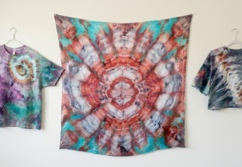 Three unique tie dye patterns side by side: a nautilus spiral shirt in teal and purple, a kaleidoscope pattern in coral and teal, and a psychedelic roll crop top in muted tones