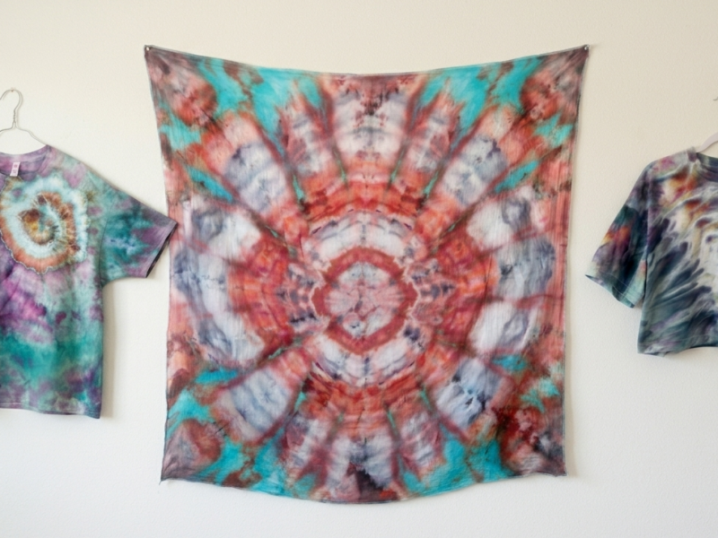 Three unique tie dye patterns side by side: a nautilus spiral shirt in teal and purple, a kaleidoscope pattern in coral and teal, and a psychedelic roll crop top in muted tones