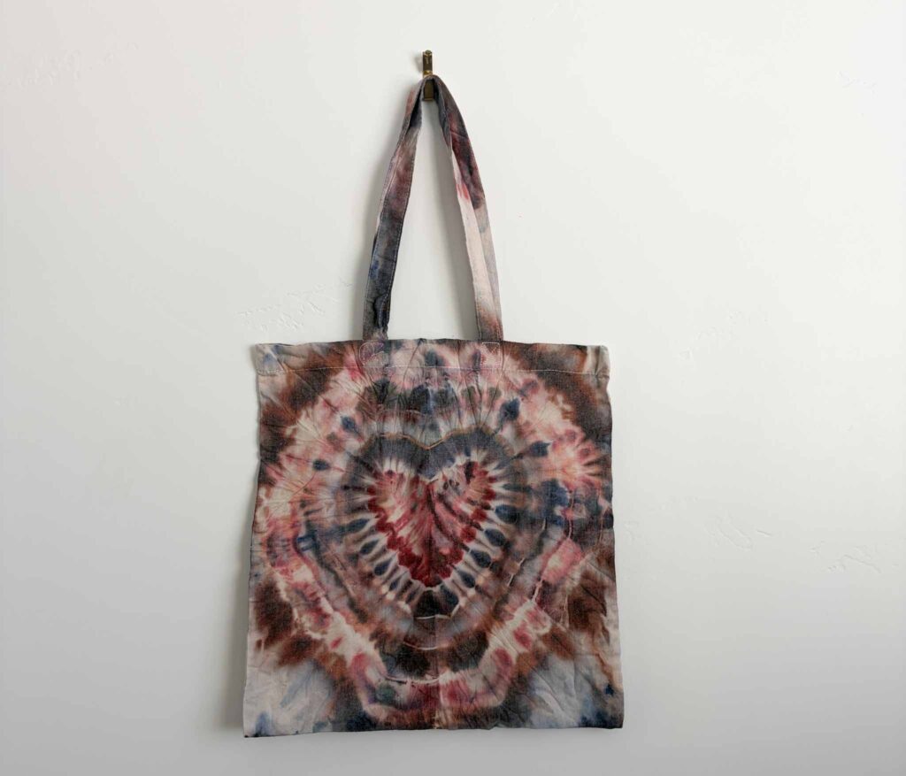 Finished ice dye tote bag with a heart shaped tie dye pattern in rust and navy
