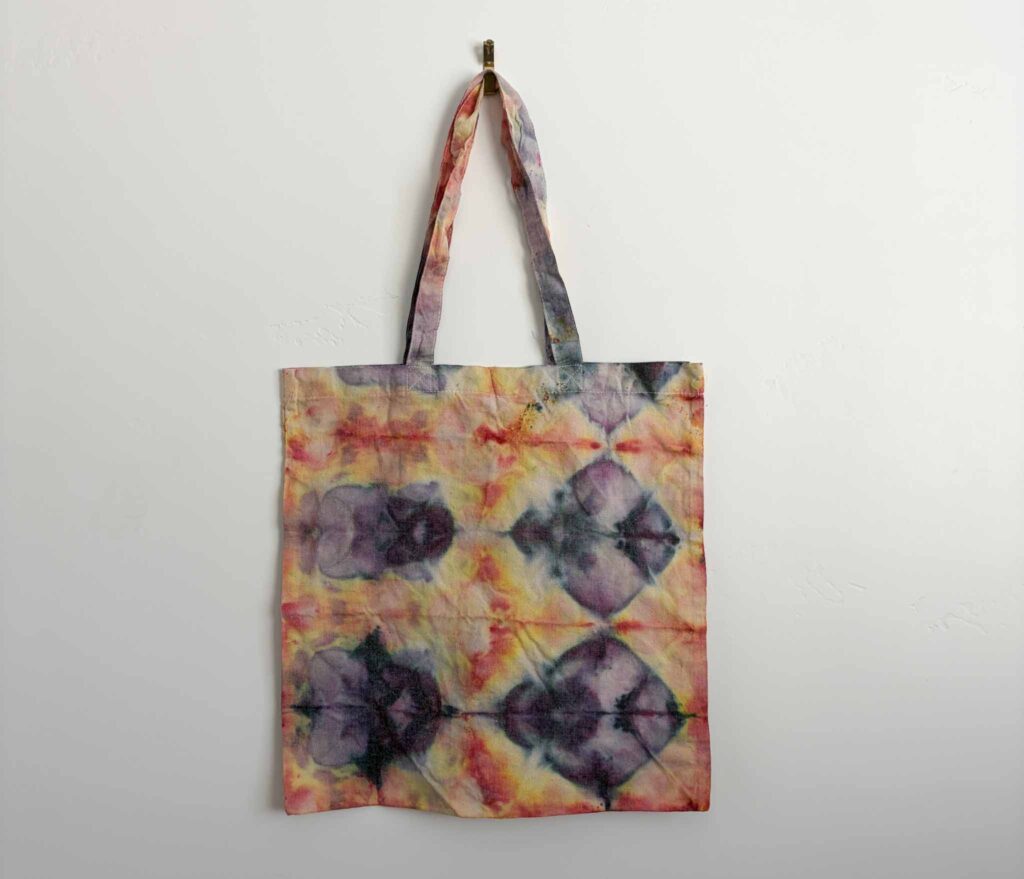 Finished ice dye shibori tote bag with a repeating diamond pattern in purple, yellow, and red