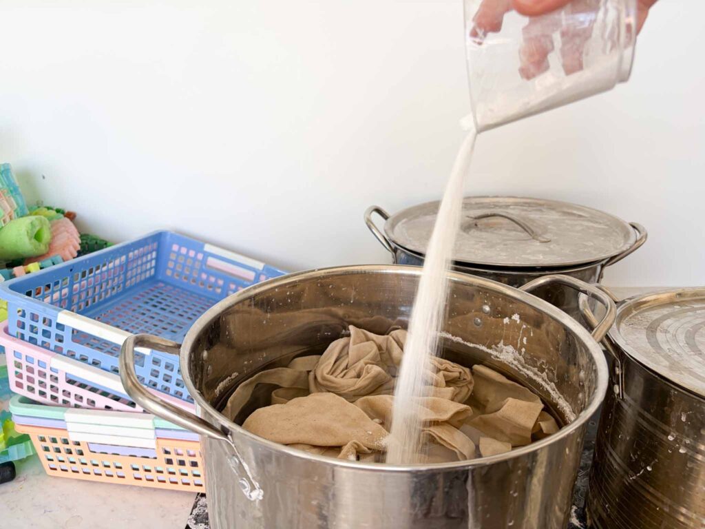 Pouring soda ash powder into a pot of water with fabric soaking for tie dye