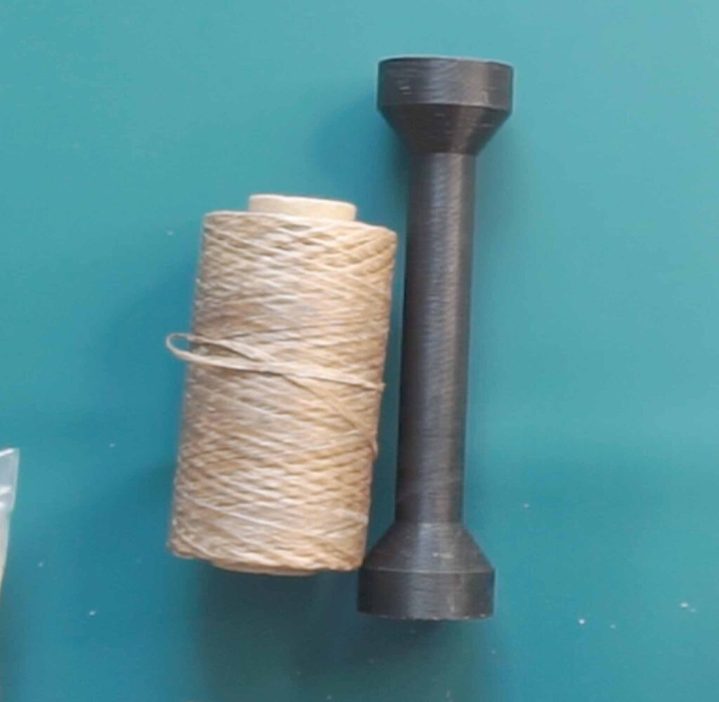 Spool of waxed sinew next to a wooden sinew puller used for tie dye