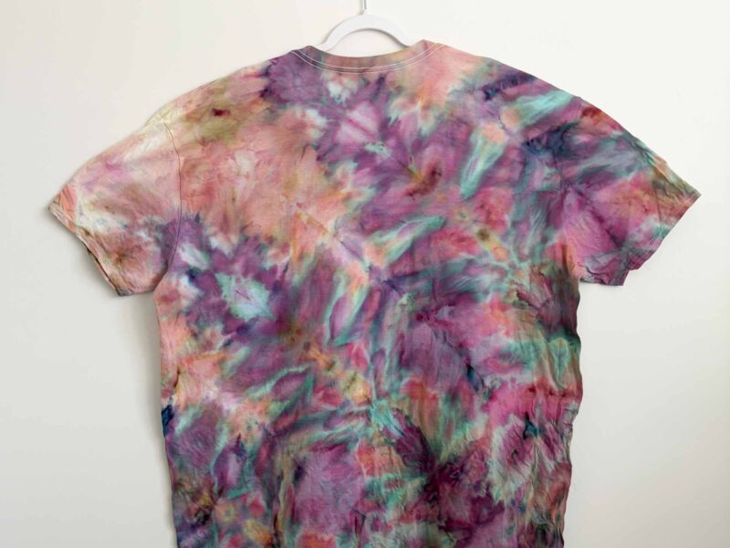 Finished fern fold ice dye shirt in pink, purple, and teal hanging on a white hanger