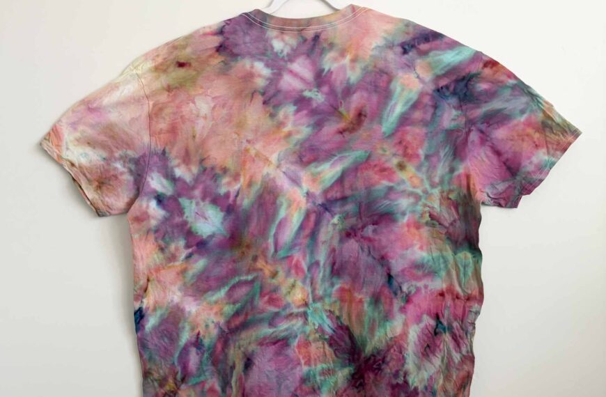 Finished fern fold ice dye shirt in pink, purple, and teal hanging on a white hanger