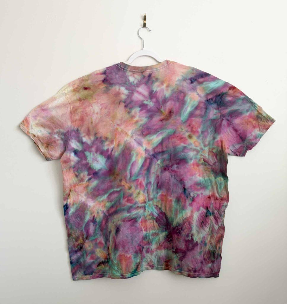Finished fern fold ice dye shirt in pink, purple, and teal hanging on a white hanger