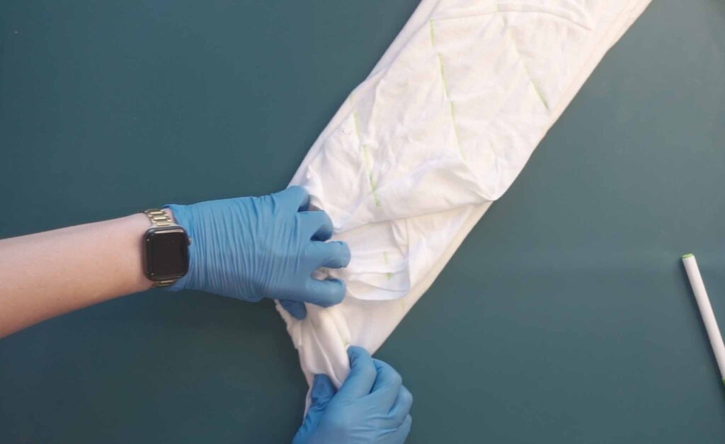 Hands in gloves securing a folded tie dye shirt with rubber bands