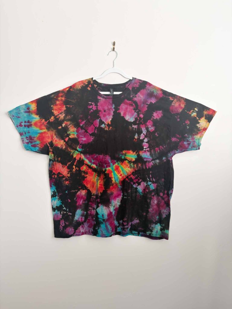 Reverse tie dye shirt with a geode pattern and bright pink, orange, and teal color against black
