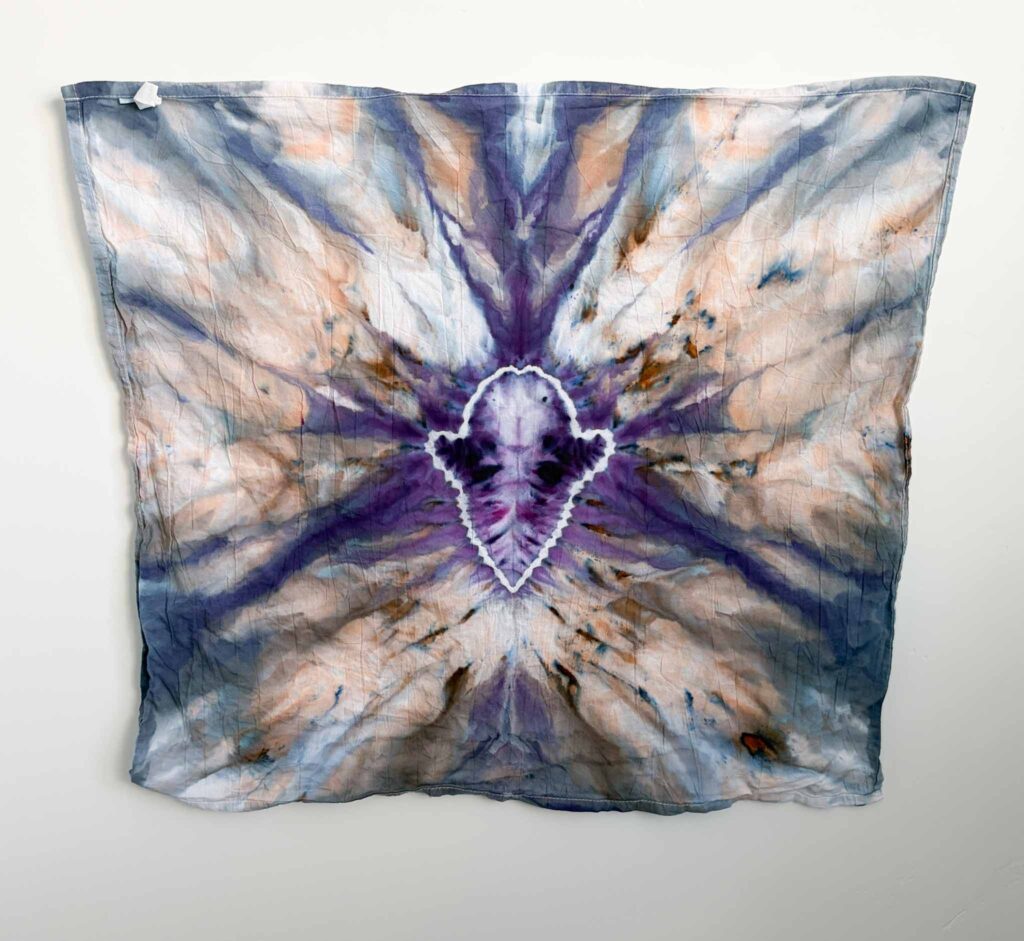 Purple ghost shape tie dye towel with a white outline and purple and blue stripes radiating over peach