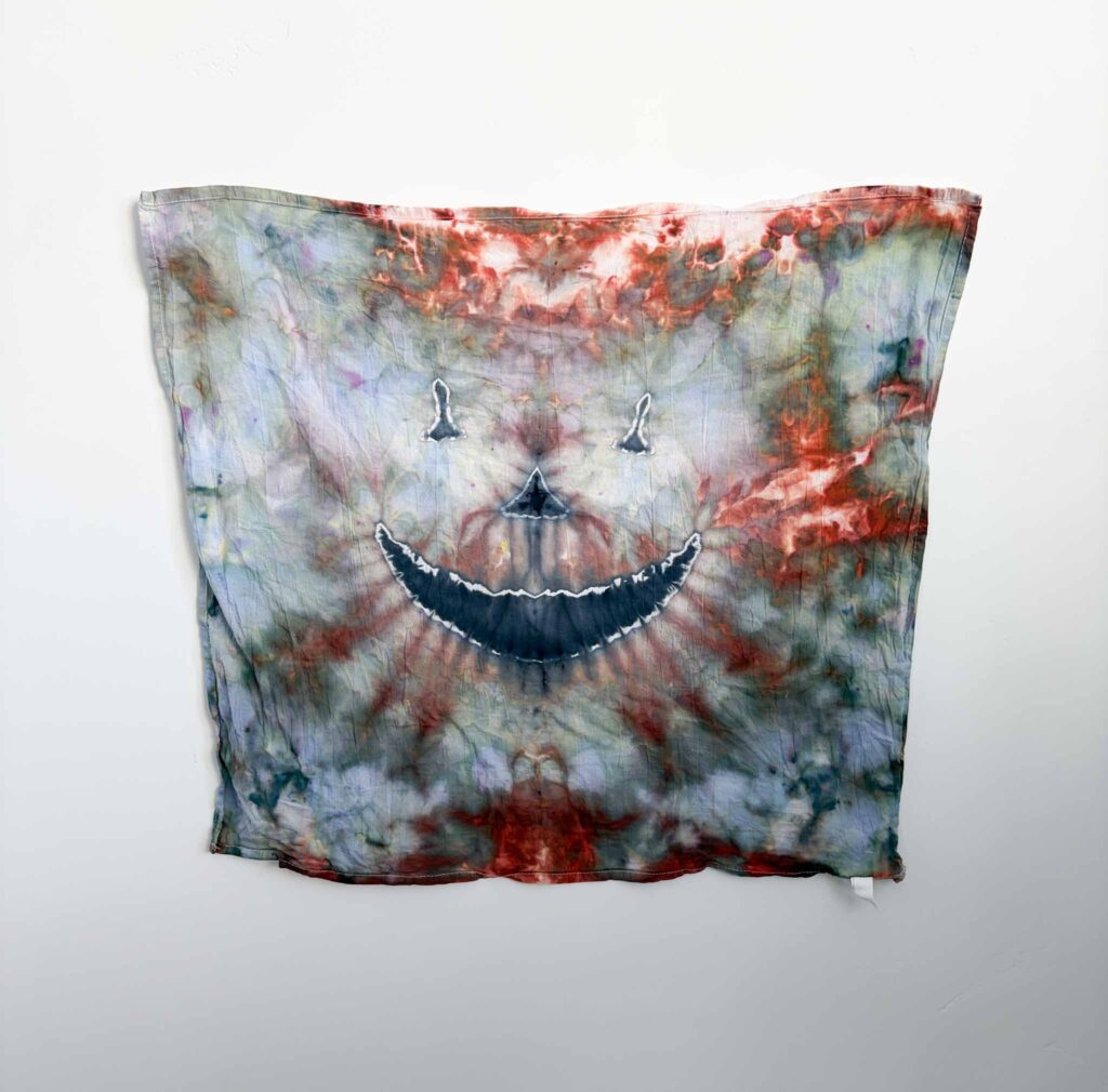 Ice dyed Halloween tie dye towel with a black jack-o’-lantern face over swirls of rust red, sage green, and blue gray